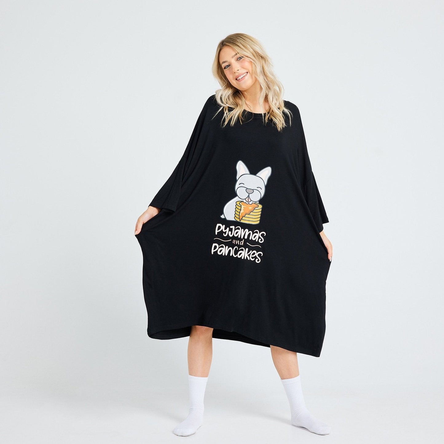 Woman wearing a black oversized dress with a cartoon bulldog holding pancakes and the text 'pyjamas and pancakes'