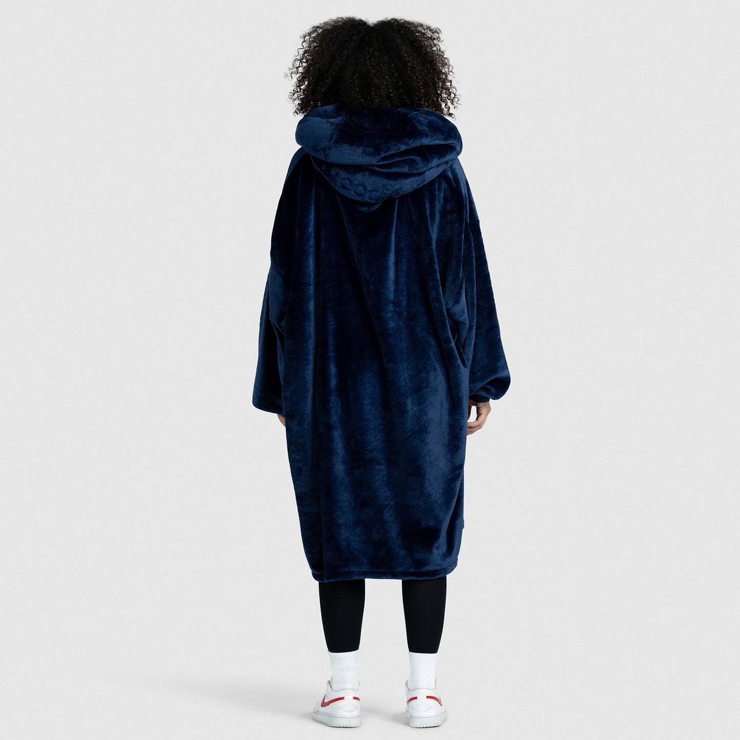 Back view of a person wearing a long, dark blue plush hooded coat, standing against a plain background. Text on image: