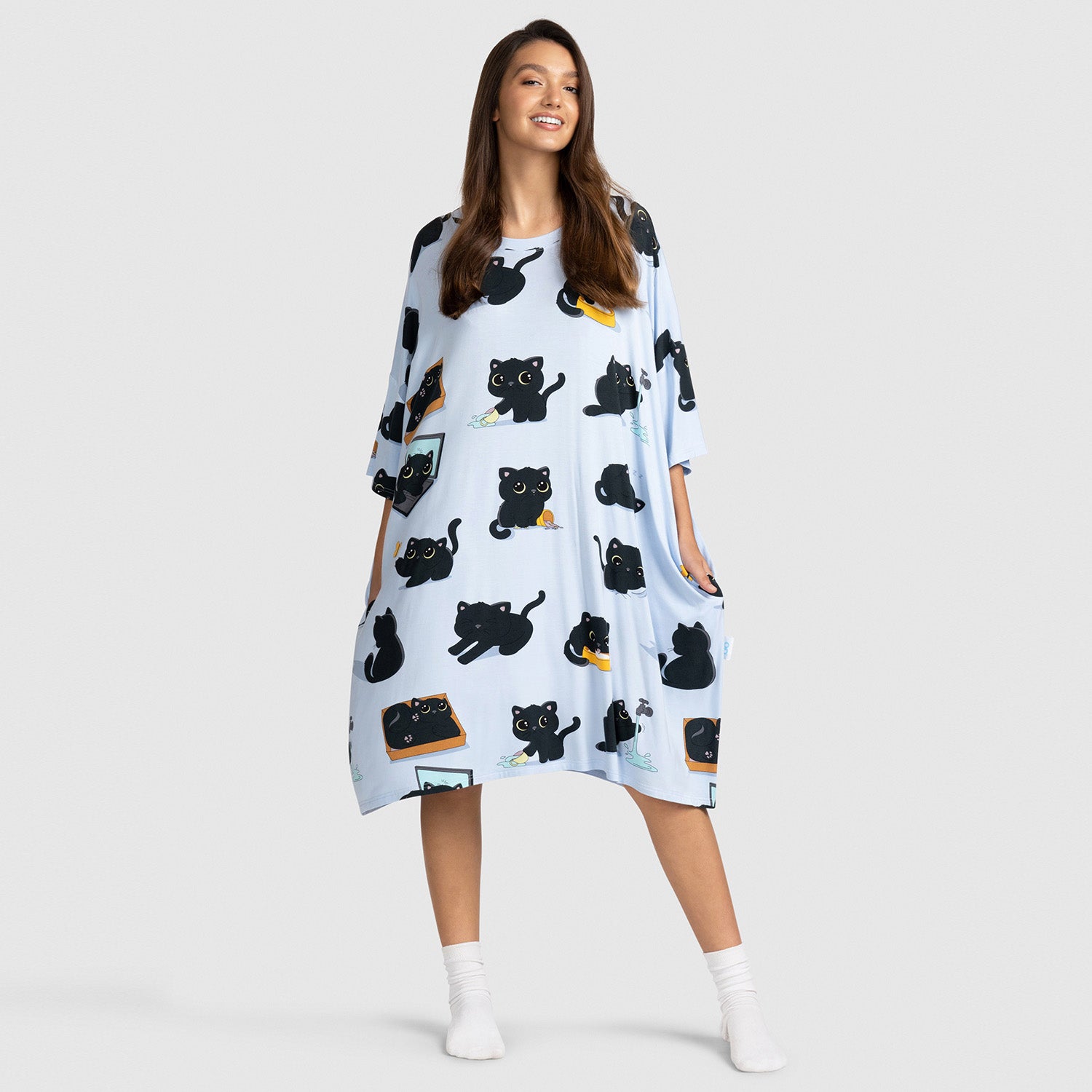 Woman wearing a light blue loose dress with black cat illustrations in various poses and expressions.