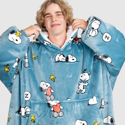 A young man wearing a blue wearable blanket covered with Snoopy and Woodstock illustrations, including Snoopy holding a heart and a 'Z' speech bubble.