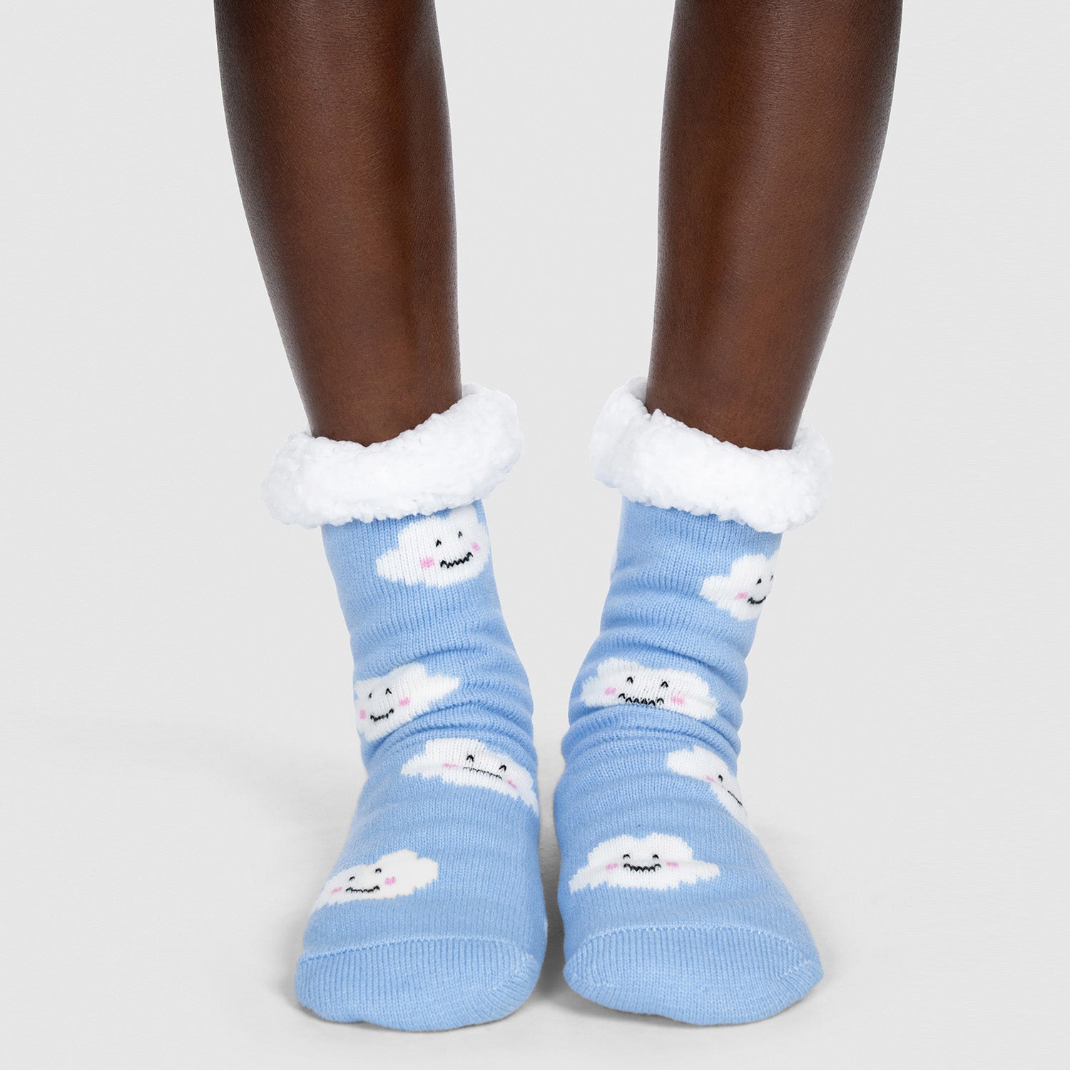 Pair of blue socks with white fluffy cuffs, decorated with smiling white cloud faces, worn on feet.