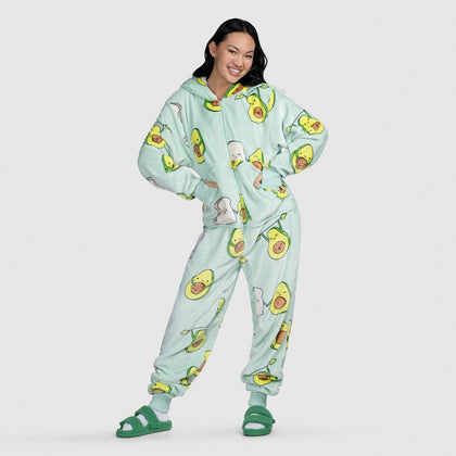Cait Lin wearing mint-green avocado-print hooded onesie with pockets and green slippers, standing hands in pockets, smiling