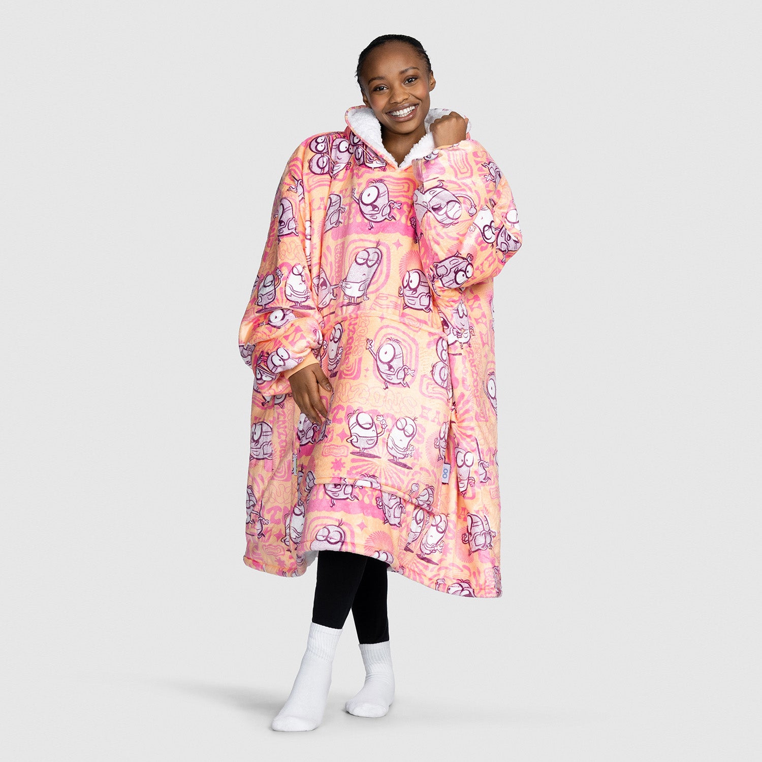 Smiling woman wearing a pink and orange fleece wearable blanket with cartoon Minions characters printed all over it
