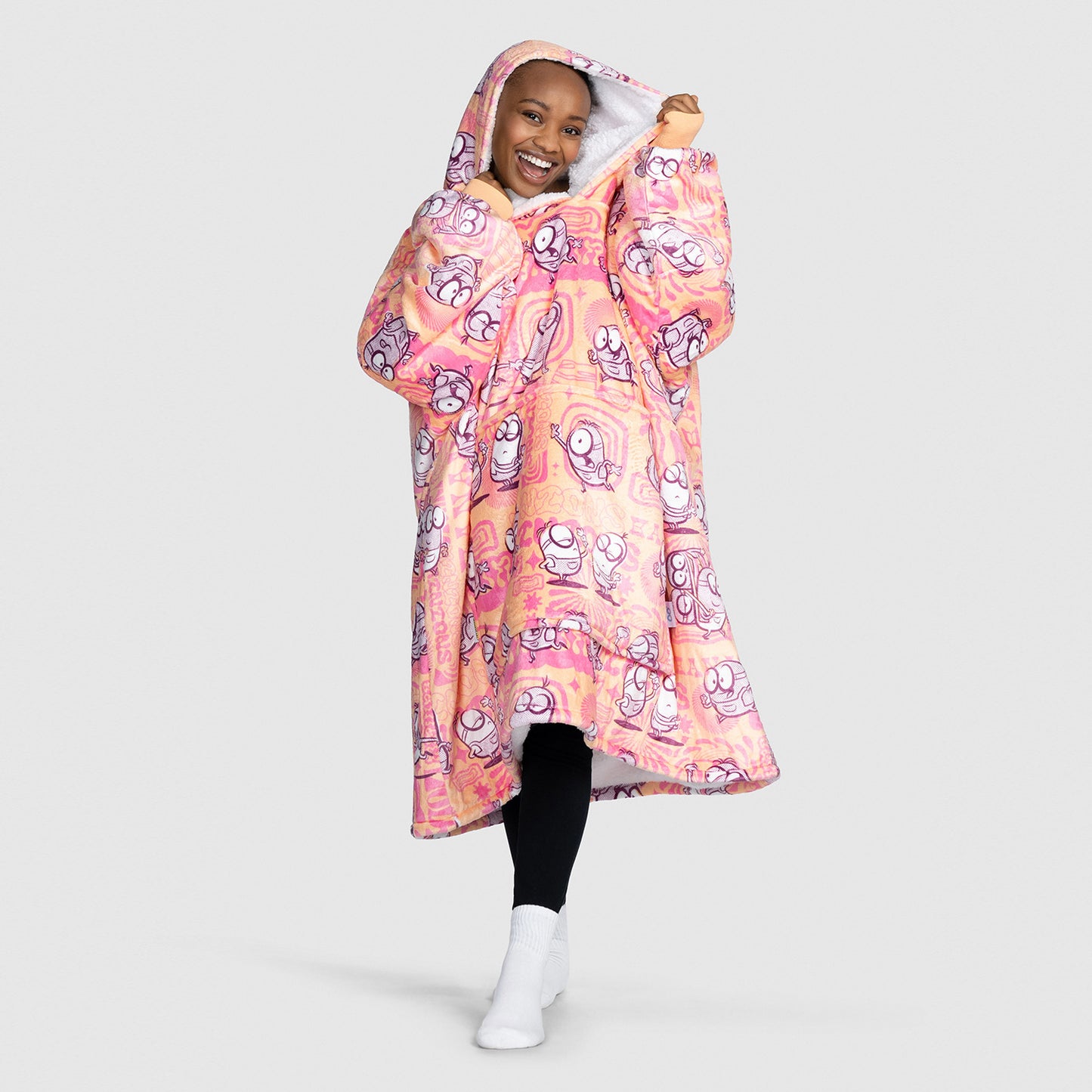 Smiling person wearing a hooded wearable blanket with pink and orange sherbert Minions pattern