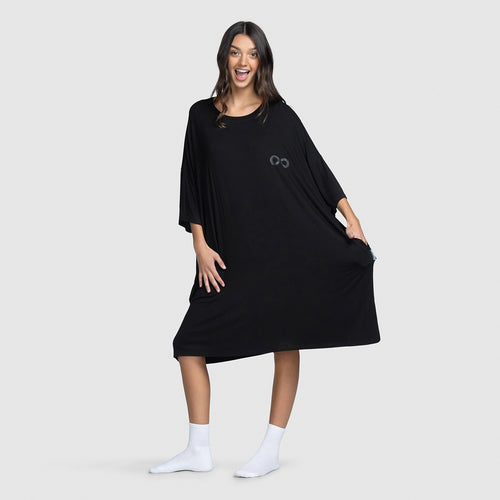 Woman smiling wearing a loose black dress and white socks, holding the dress out to the side