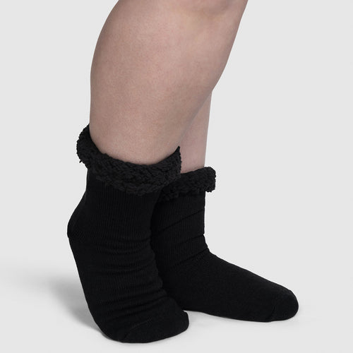 Pair of black socks with fuzzy cuffs worn on feet against a plain background