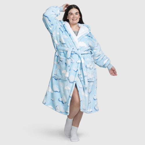Woman wearing a blue robe with white cloud patterns, smiling and posing with one hand on her head and one arm extended.