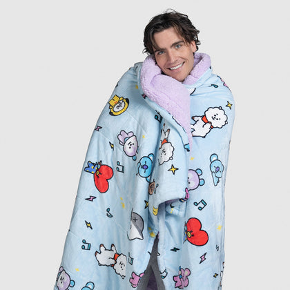 Man wrapped in a light blue BT21 character blanket with purple lining, smiling at the camera