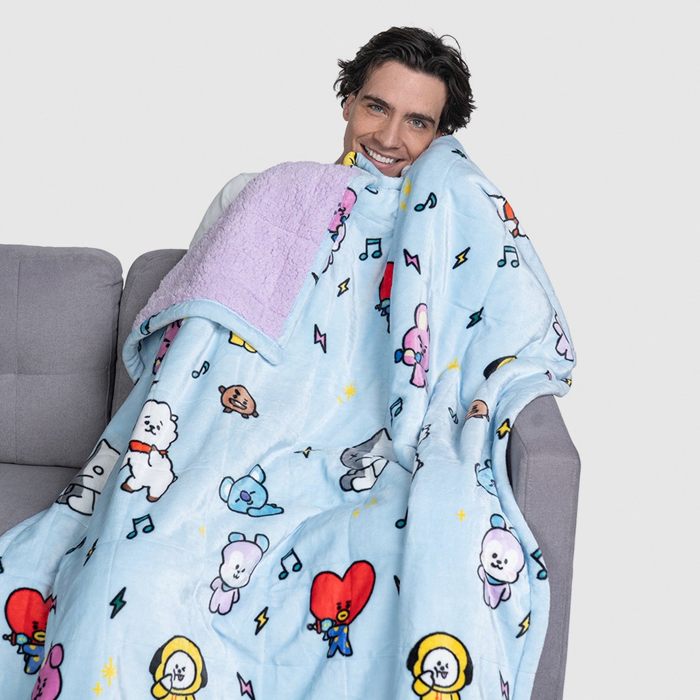 Man wrapped in a BT21 character blanket featuring colorful cartoon figures on light blue fabric