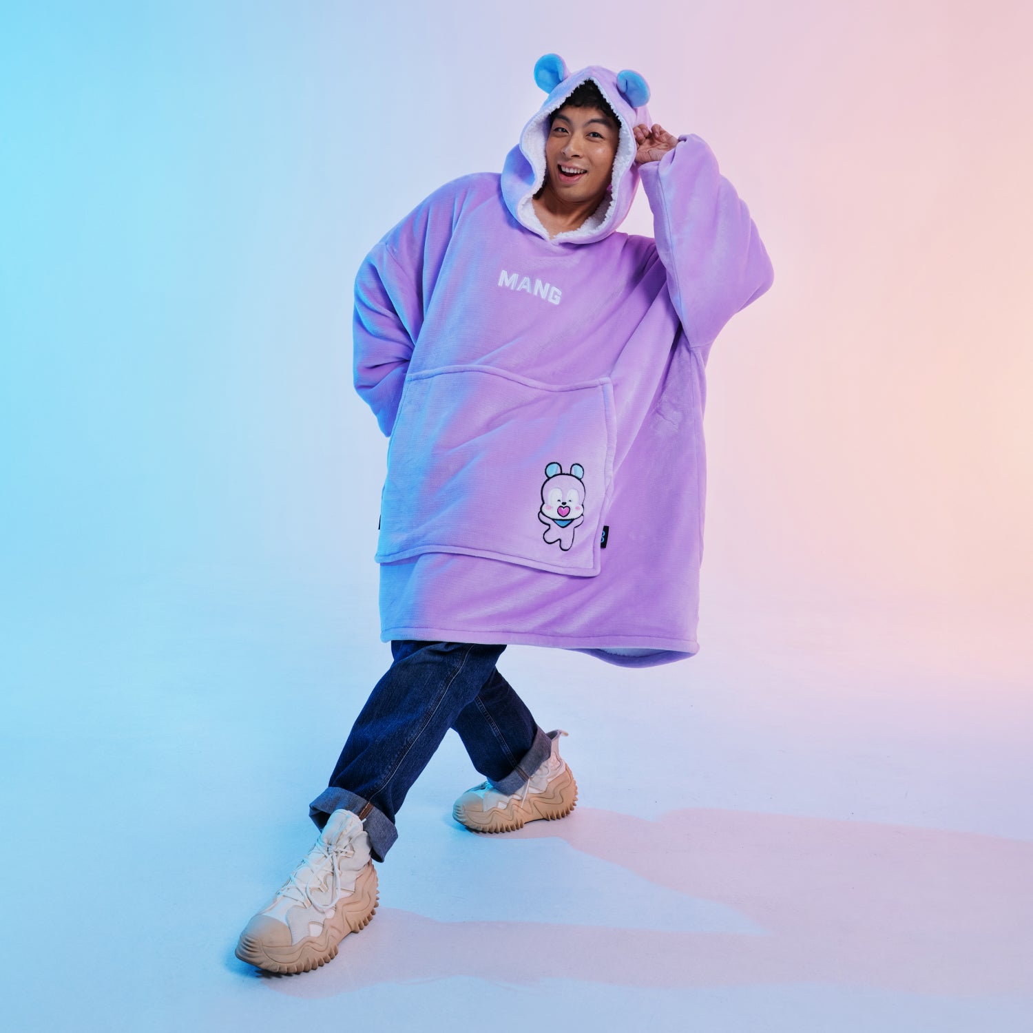 Person wearing a purple oversized hoodie with hood ears, 'MANG' text, and a cartoon character on the front pocket.