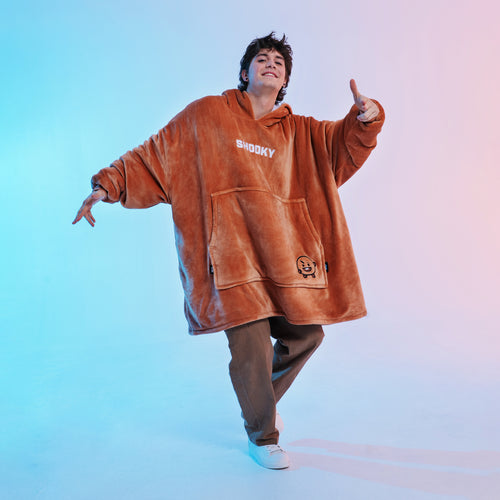 Person wearing a brown oversized hoodie with 'SHOOKY' text and a small character logo, posing with one hand raised