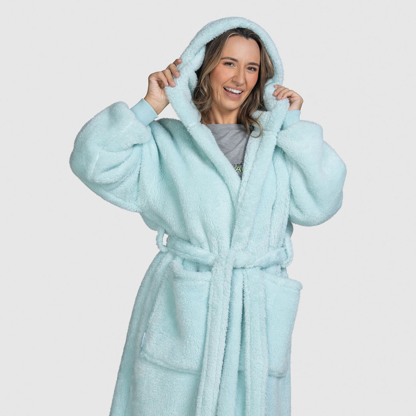 Smiling woman wearing a light blue fluffy hooded robe, holding the hood with both hands
