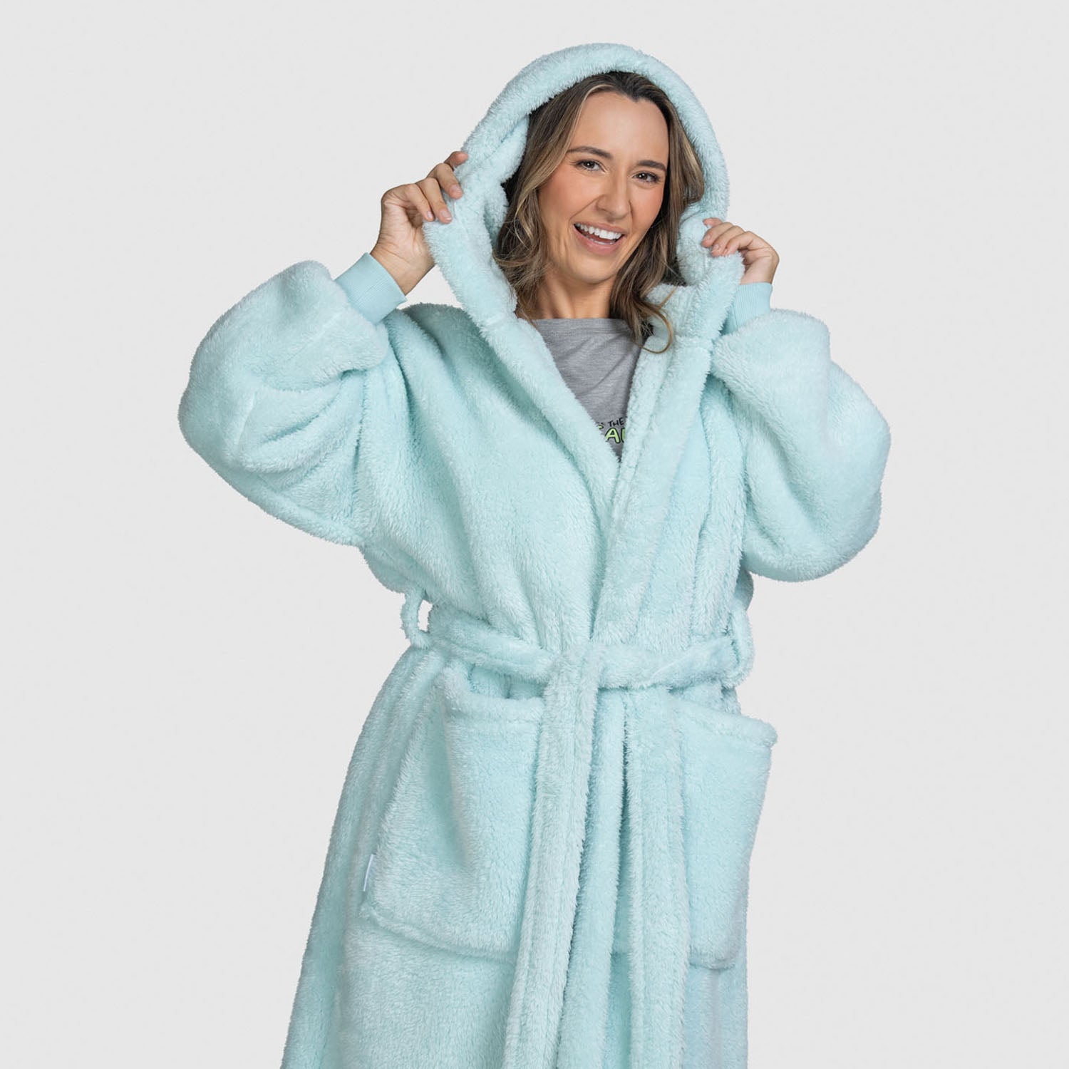 Smiling woman wearing a light blue fluffy hooded robe, holding the hood with both hands