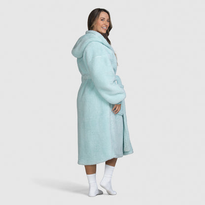 Woman wearing a light blue hooded robe standing and smiling, shown from the side