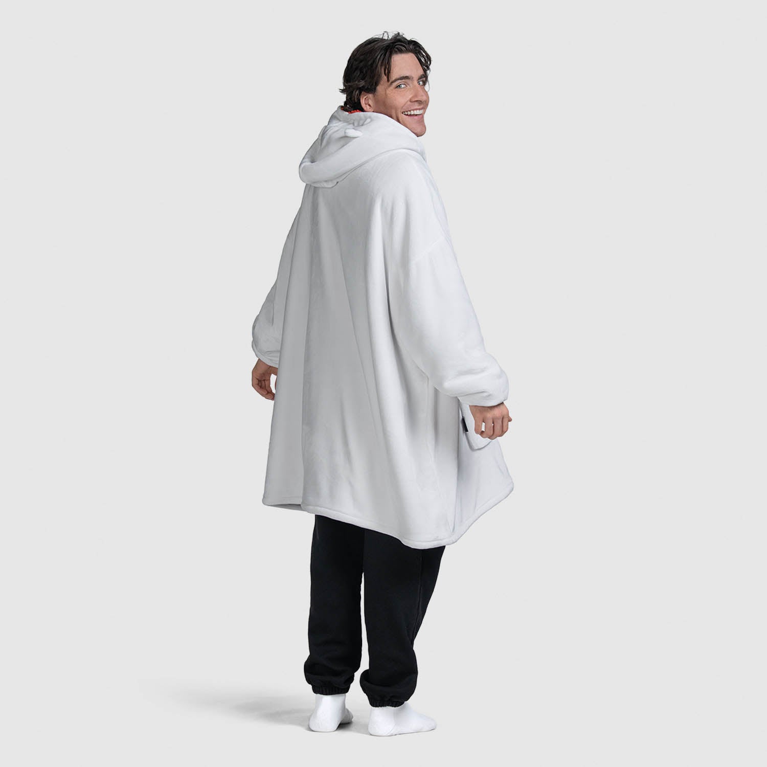 Man wearing a white oversized hoodie with a hood, smiling and looking back