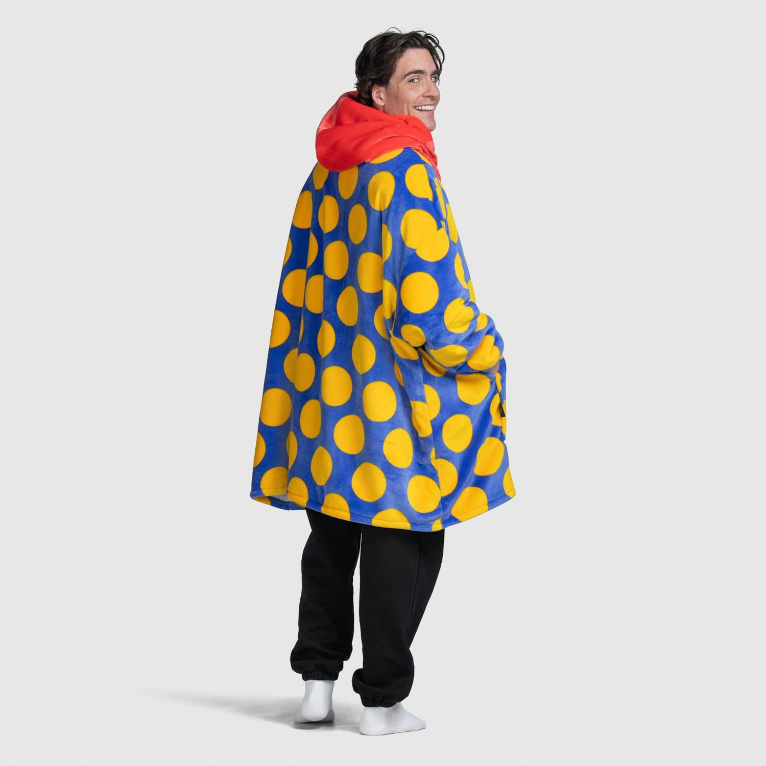 Man wearing a blue coat with large yellow polka dots and a red hood, smiling and looking back
