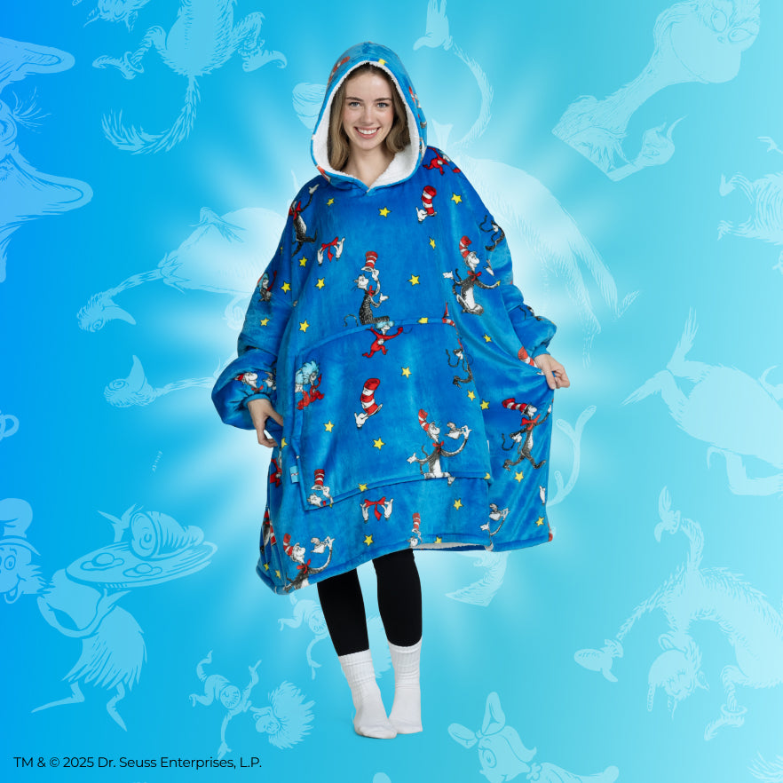 Woman wearing a blue hooded blanket with Cat in the Hat characters printed, standing against a blue background with faint Cat in the Hat illustrations.