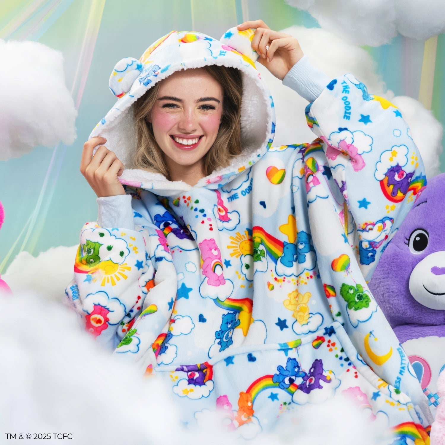 Smiling woman wearing a colorful Care Bears-themed oversized hoodie with ears on the hood