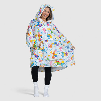 Woman wearing an oversized hoodie blanket with Care Bears characters, rainbows, and clouds pattern, smiling and posing with hands in pockets.