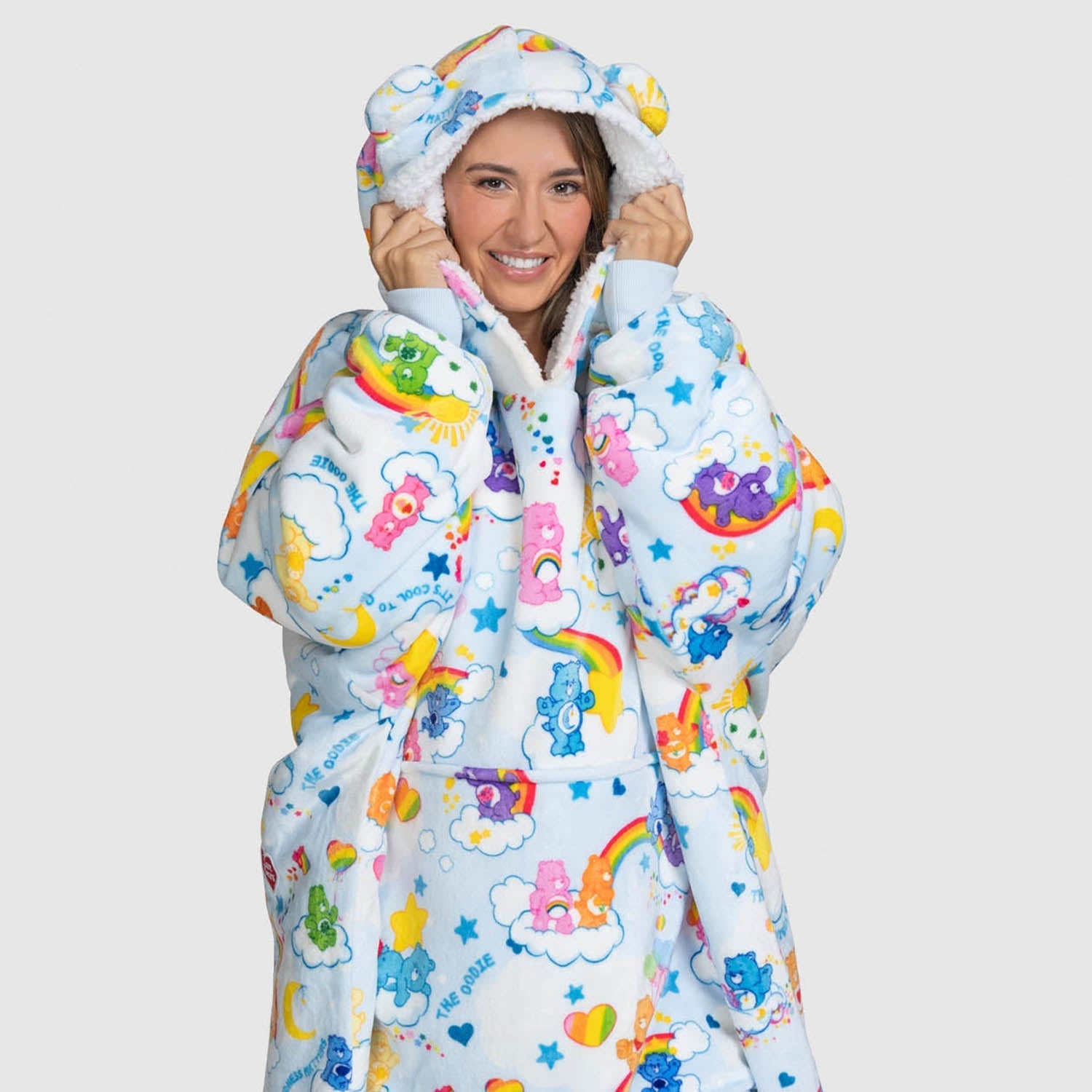 Smiling woman wearing a colorful Care Bears-themed hooded jacket with clouds, stars, rainbows, and Care Bears characters