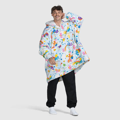 A smiling man wearing a colorful oversized hoodie with Care Bears and clouds pattern, standing against a plain background.