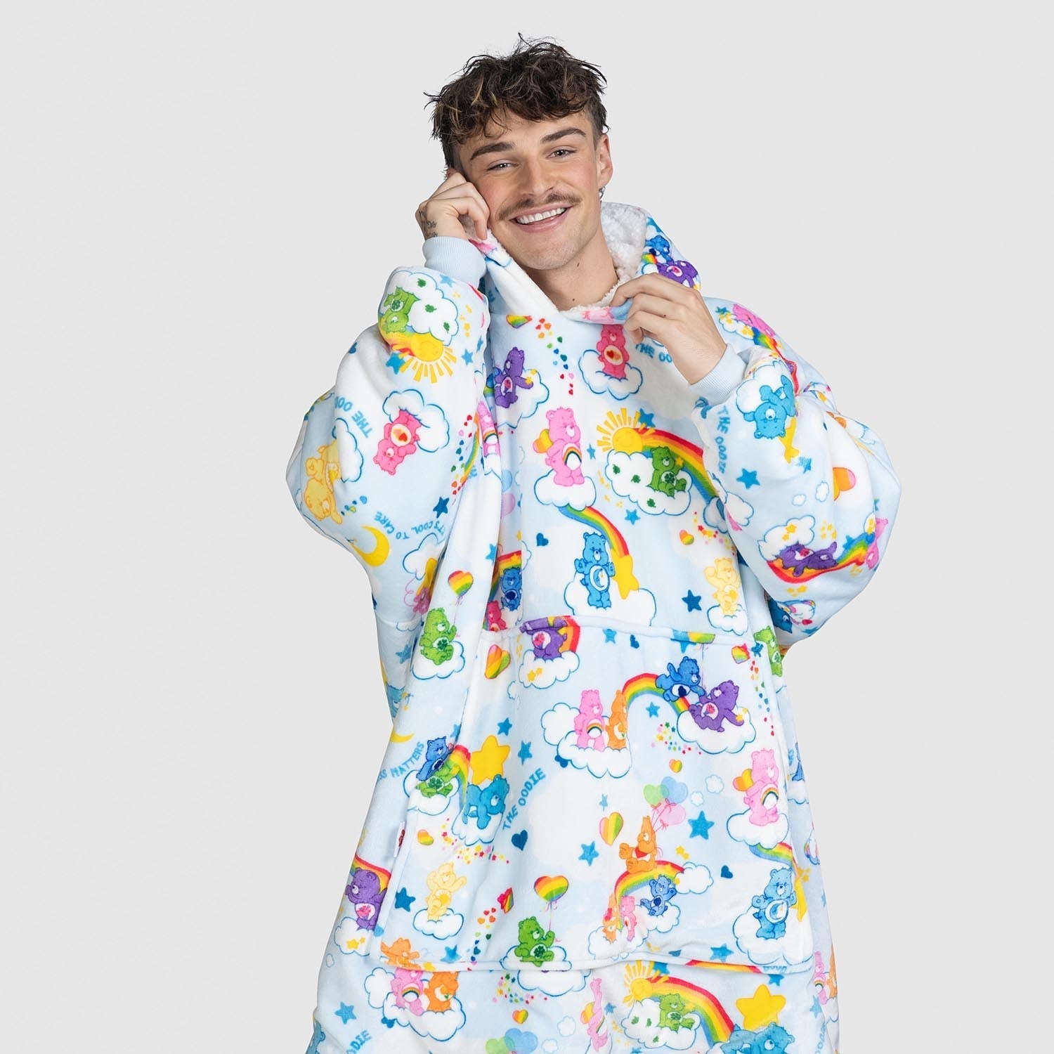 Young man wearing a colorful Care Bears-themed hoodie and matching pants with clouds, rainbows, and Care Bears characters all over.