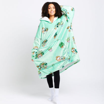 Person wearing a mint green oversized hoodie blanket with cartoon plant and character prints, standing and smiling.