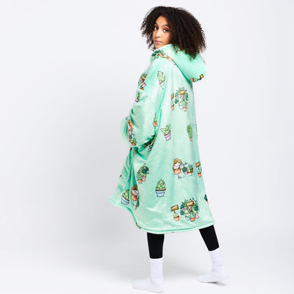 Woman wearing a mint green hooded robe with cartoon plant designs, standing and looking over her shoulder.