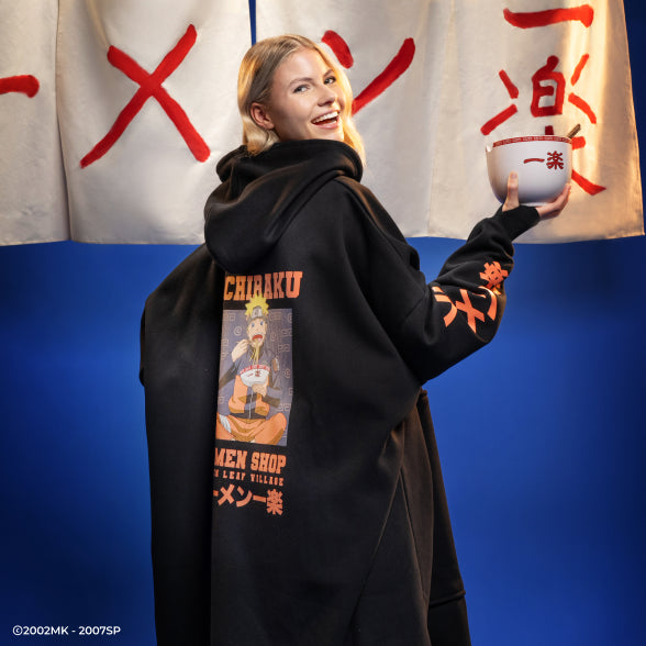 Smiling woman holding a ramen bowl with Japanese characters, wearing a black hoodie featuring Naruto character and text 'Ichiraku Ramen Shop Hidden Leaf Village'