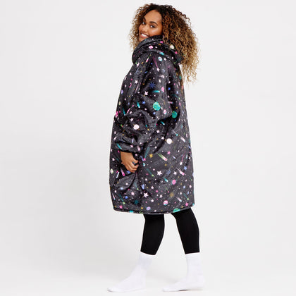 Woman wearing a black oversized coat with colorful space-themed pattern including stars and planets, standing sideways and smiling.