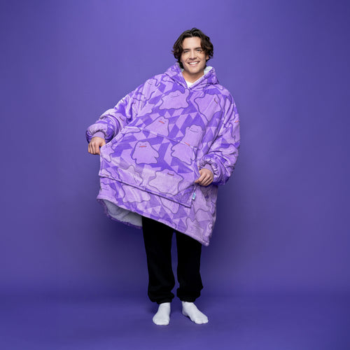 Person wearing a large purple hoodie blanket covered in Pokémon Ditto patterns, standing barefoot against a purple background