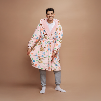 Man wearing a pink robe patterned with Pokémon Eevee and colorful flowers, standing and smiling against a beige background.
