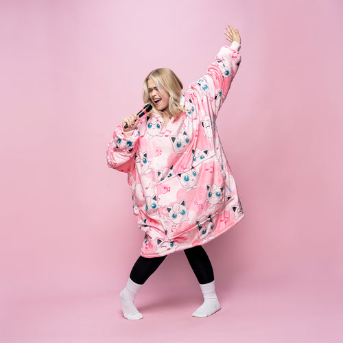 Woman singing into a microphone wearing a pink oversized garment patterned with multiple Jigglypuff faces on a pink background