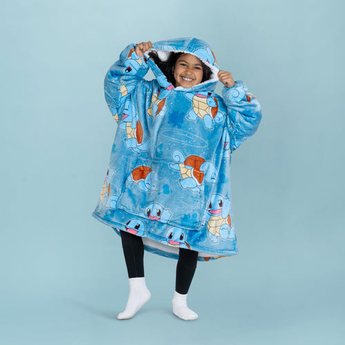 Child wearing a large blue hooded blanket covered with multiple images of Pokémon Squirtle, smiling and holding the hood up.