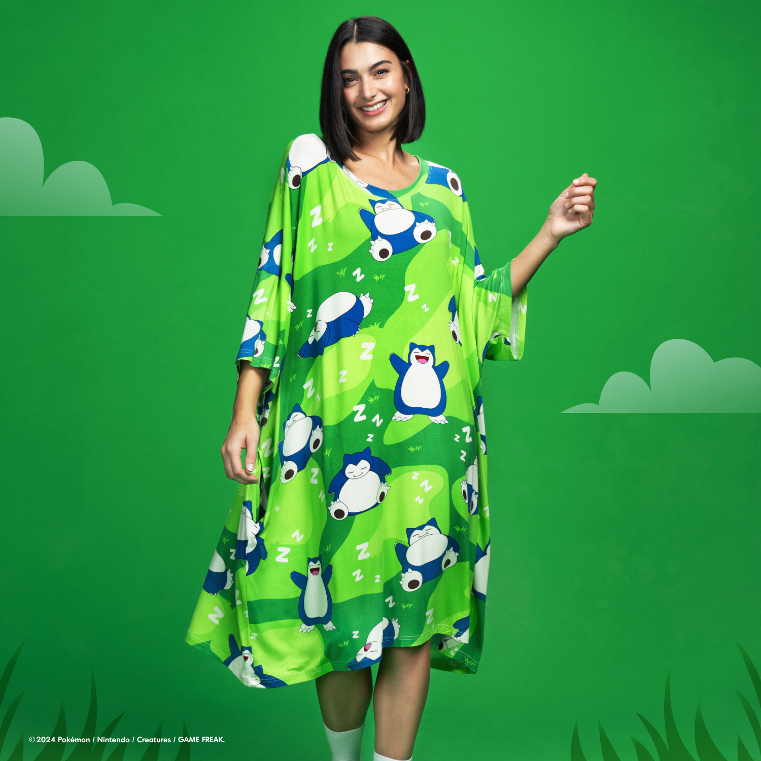 Woman wearing a green dress patterned with multiple Snorlax Pokémon and white 'Z' symbols on a green background with stylized clouds and grass.