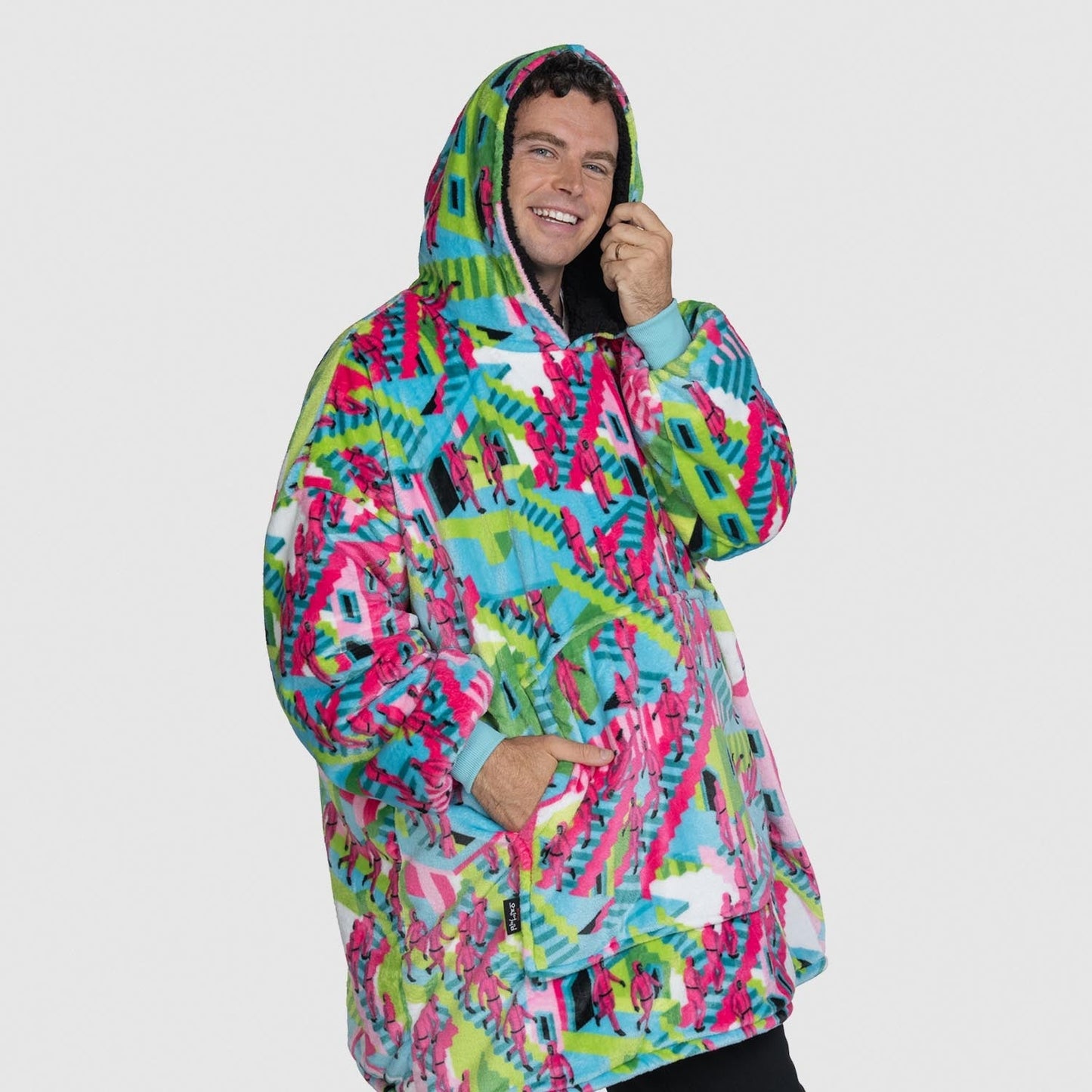 Man wearing a colorful patterned oversized hoodie, smiling, with text 'size: Jake is 191cm wearing a size OOD'. size: Jake is 191cm wearing a size OOD