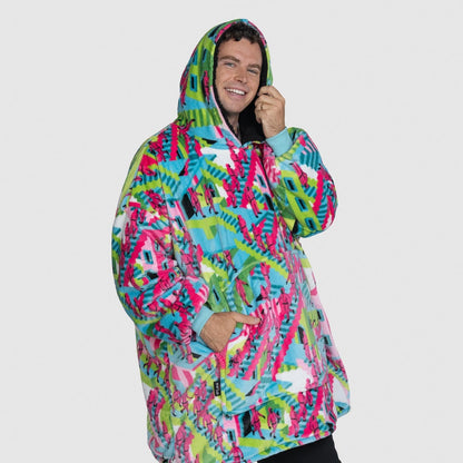 Man wearing a colorful patterned oversized hoodie, smiling, with text 'size: Jake is 191cm wearing a size OOD'. size: Jake is 191cm wearing a size OOD