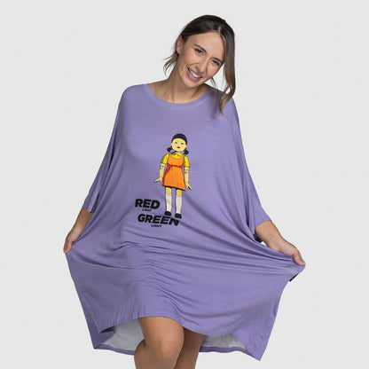 Woman smiling and holding out sides of a loose purple dress with a graphic of a doll and text "RED GREEN"; model is 5'7" wearing size S-XL. size: Danni is 5'7" wearing a size S-XL