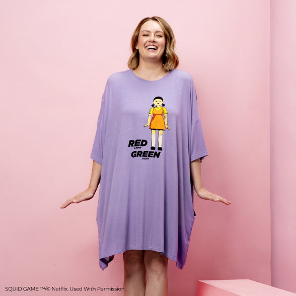 Woman wearing a purple dress with a graphic of a doll and the words 'RED LIGHT GREEN LIGHT' from Squid Game.