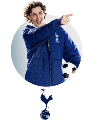 Young man in blue Tottenham Hotspur jacket holding a soccer ball and pointing forward
