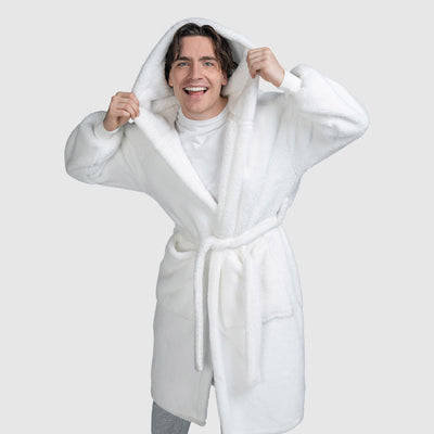 Smiling man wearing a white hooded bathrobe with a belt, holding the hood with both hands.