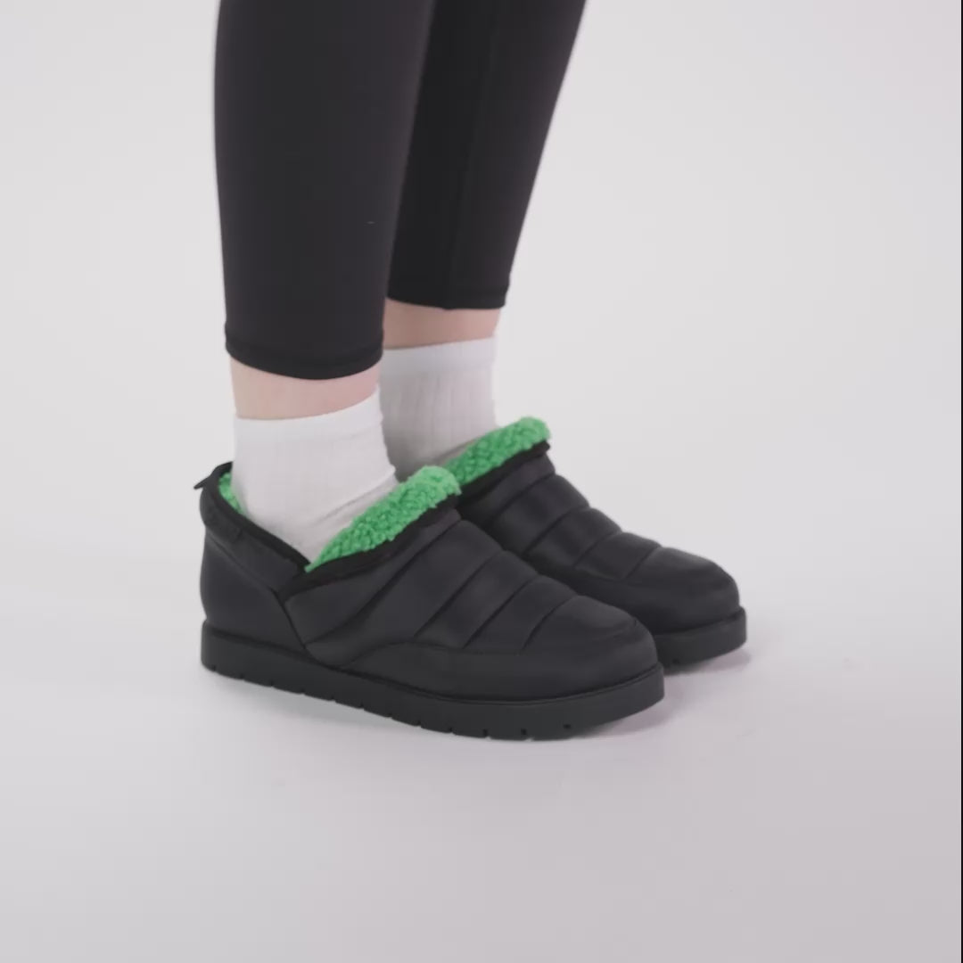 Black puffer slip-on shoes with green fleece lining worn with white socks