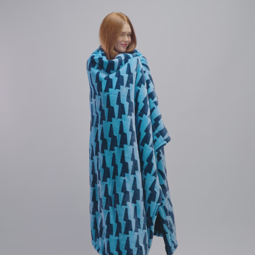 Woman wrapped in a blue blanket with a geometric pattern, smiling and looking to the side.