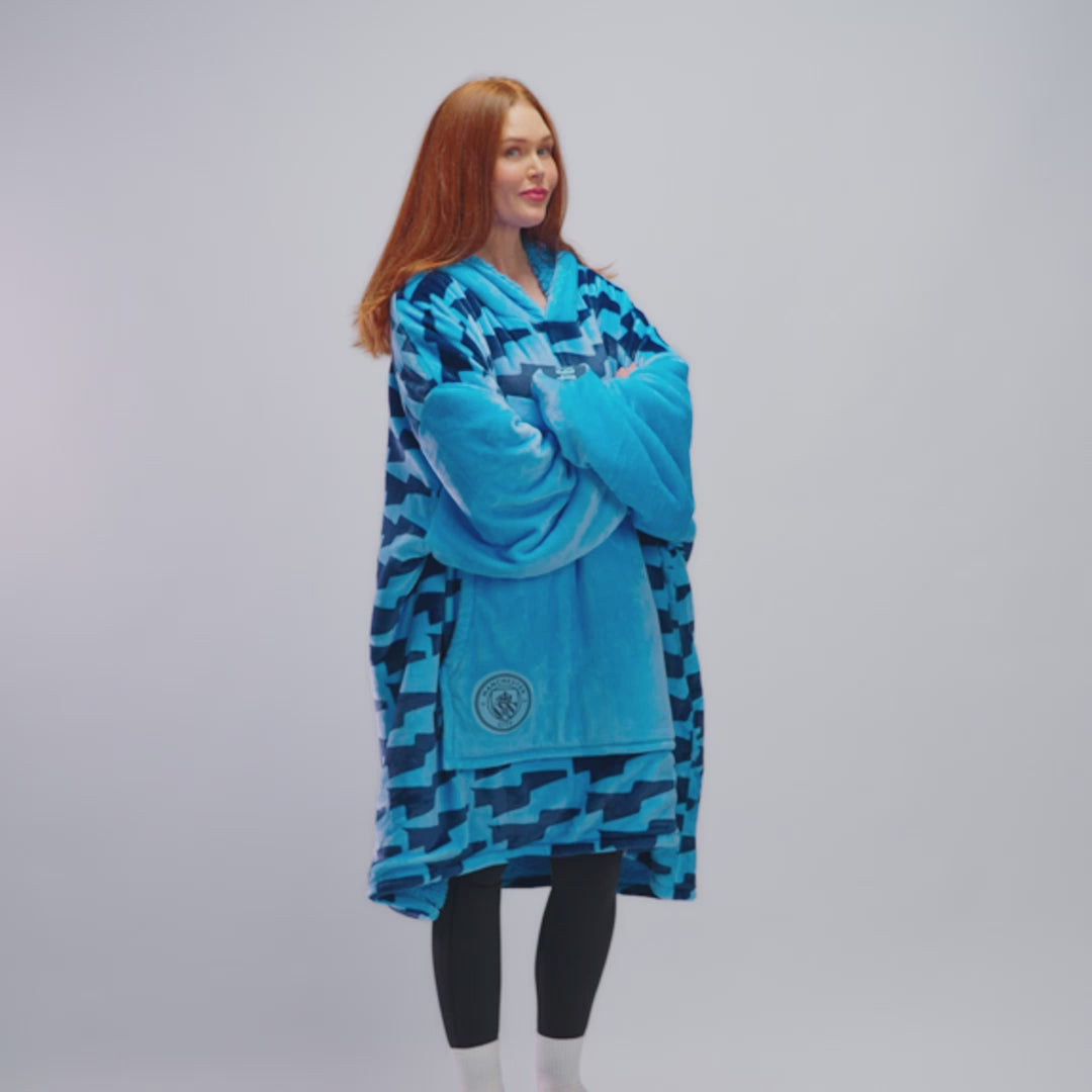 Woman wearing a blue oversized Manchester City fleece garment with logo on front pocket