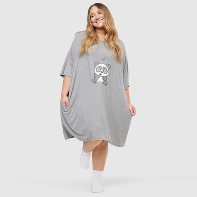 Woman wearing a loose gray dress with a cartoon panda holding bamboo printed on the front, smiling and posing with one foot raised, wearing white socks.