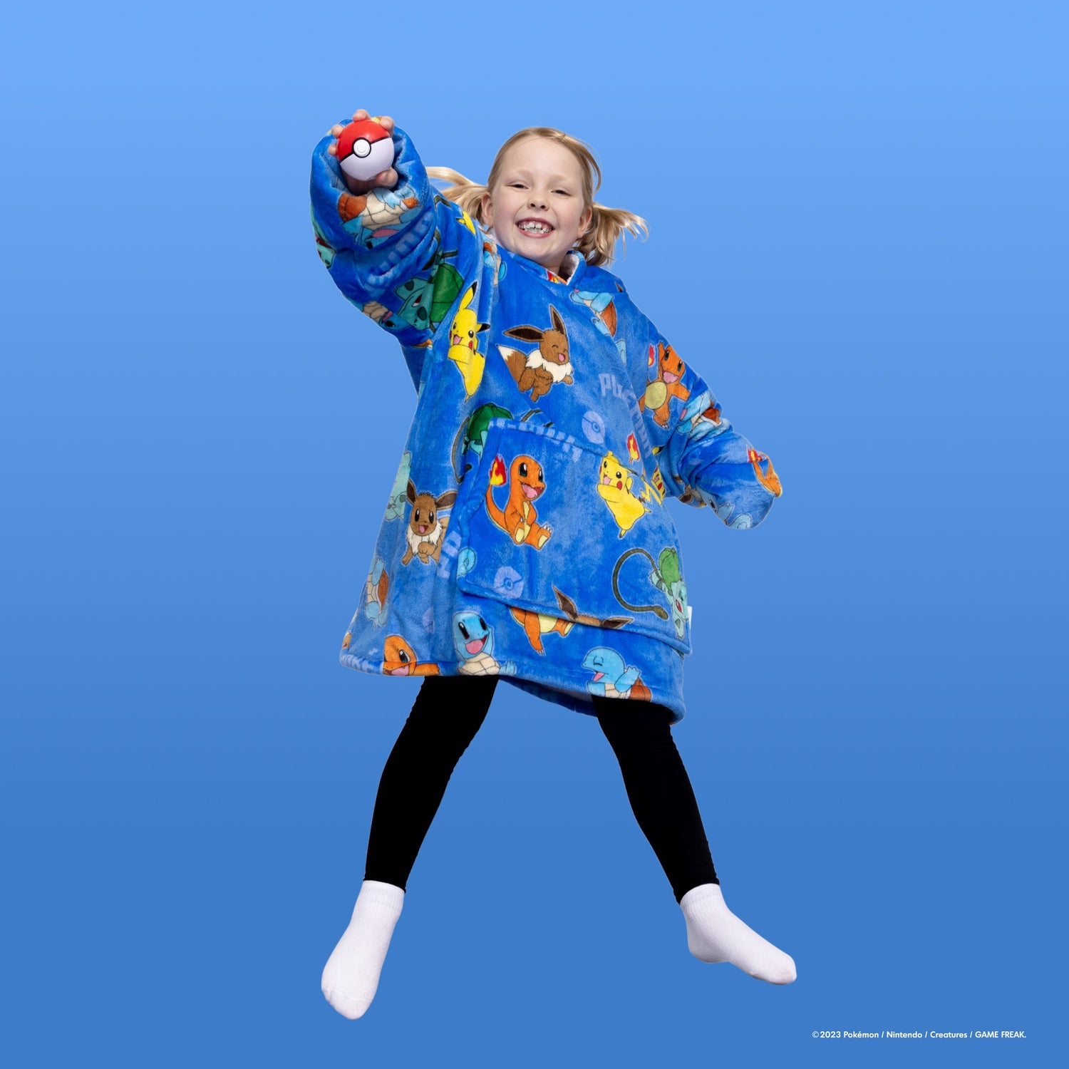 Child jumping wearing a blue Pokémon-themed hoodie with Pikachu, Eevee, Charmander, and other Pokémon, holding a Poké Ball in hand