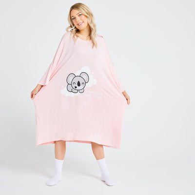 Woman wearing a pink oversized garment with a smiling koala graphic and text 'I Need Some Koala-ty Sleep'