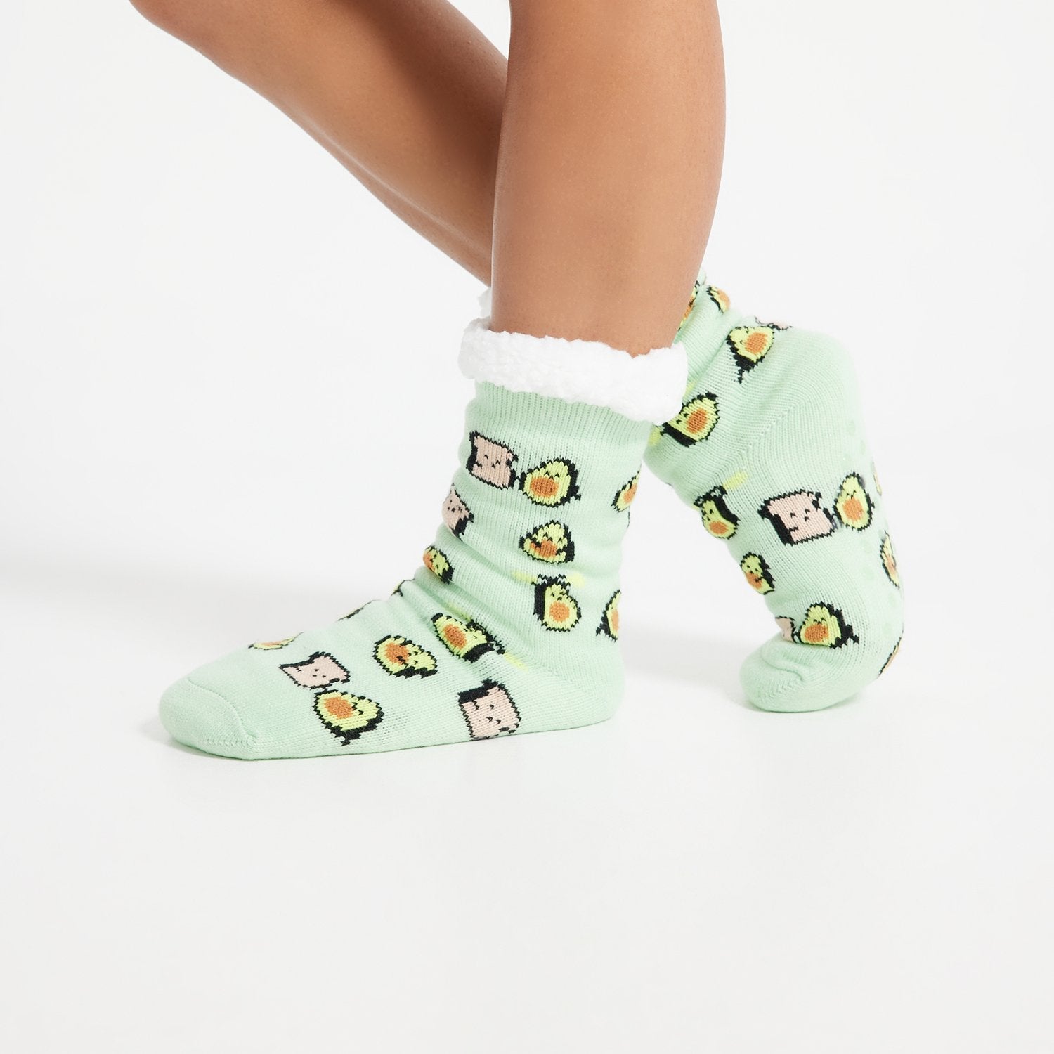 Feet wearing light green socks patterned with avocados and toast, with white fuzzy cuffs.