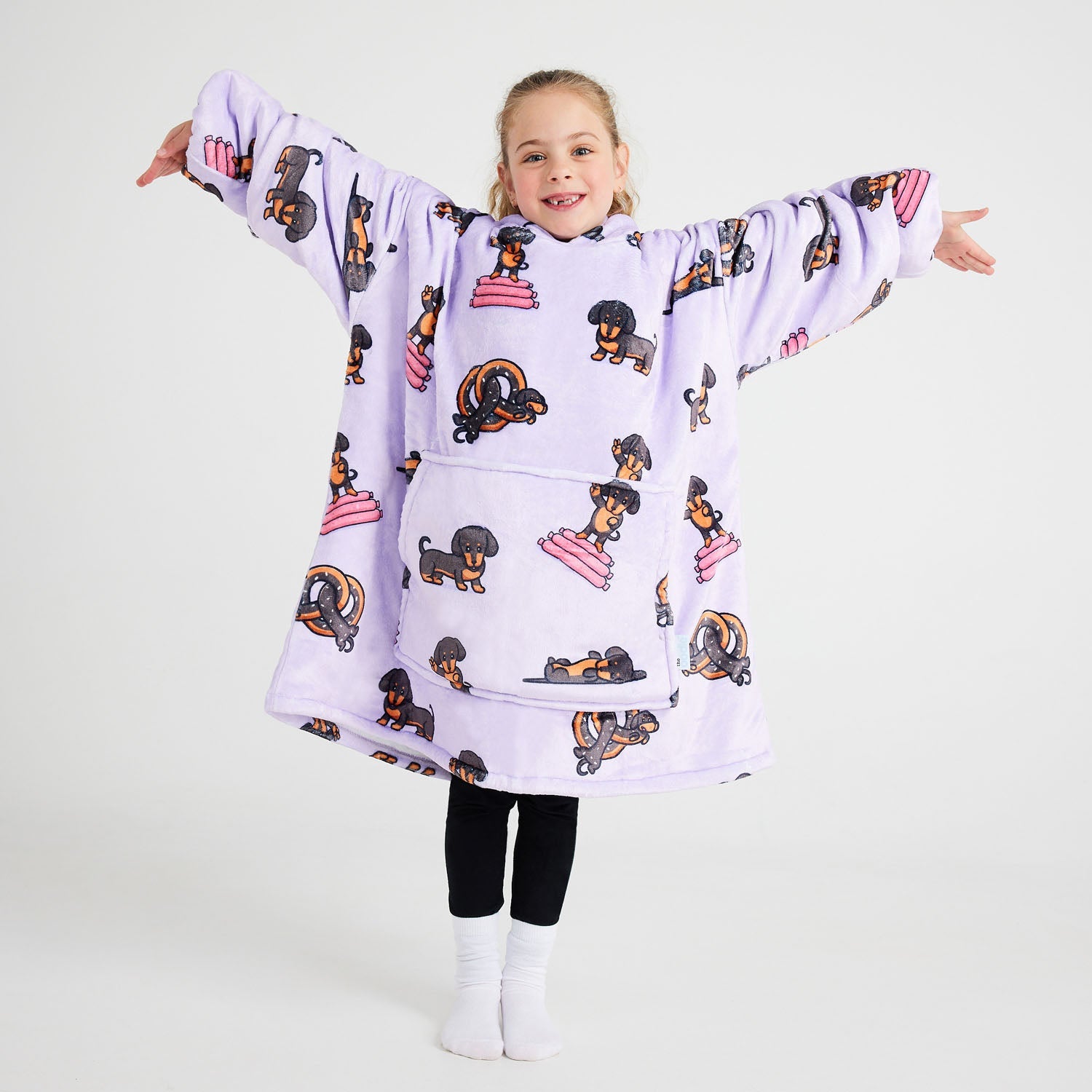 Child wearing a purple oversized hoodie with dachshund dog prints, standing with arms outstretched and smiling.