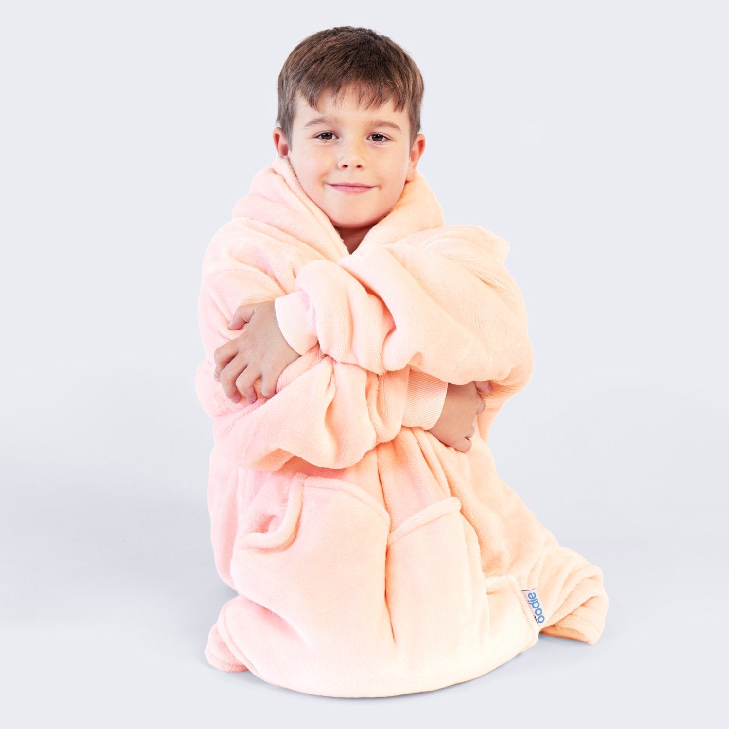 Child wrapped in a soft peach-colored wearable blanket with a visible tag reading 'poodie'.